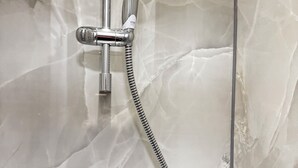 En dusch med ett duschhuvud och en slang som man kan hålla i handen, monterat på en vägg med ett kakelmönster som liknar marmor.
