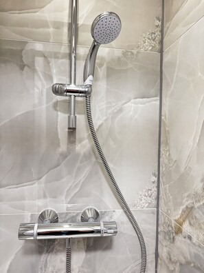 Eine Dusche mit Handbrause und Duschschlauch, an einer Wand mit einem marmorähnlichen Muster.