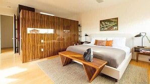 Un dormitorio moderno con cama, mesitas de noche, un banco y un separador de madera.