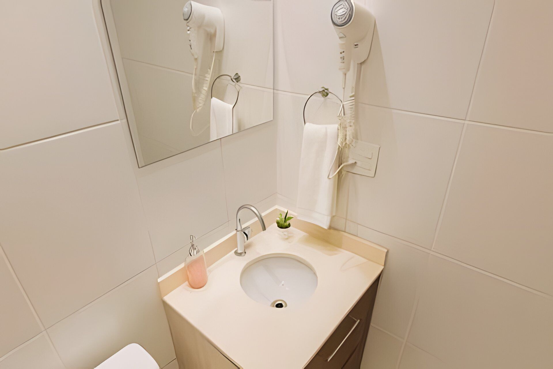 Casa de banho com lavatório, espelho, porta-toalhas e secador de cabelo.
