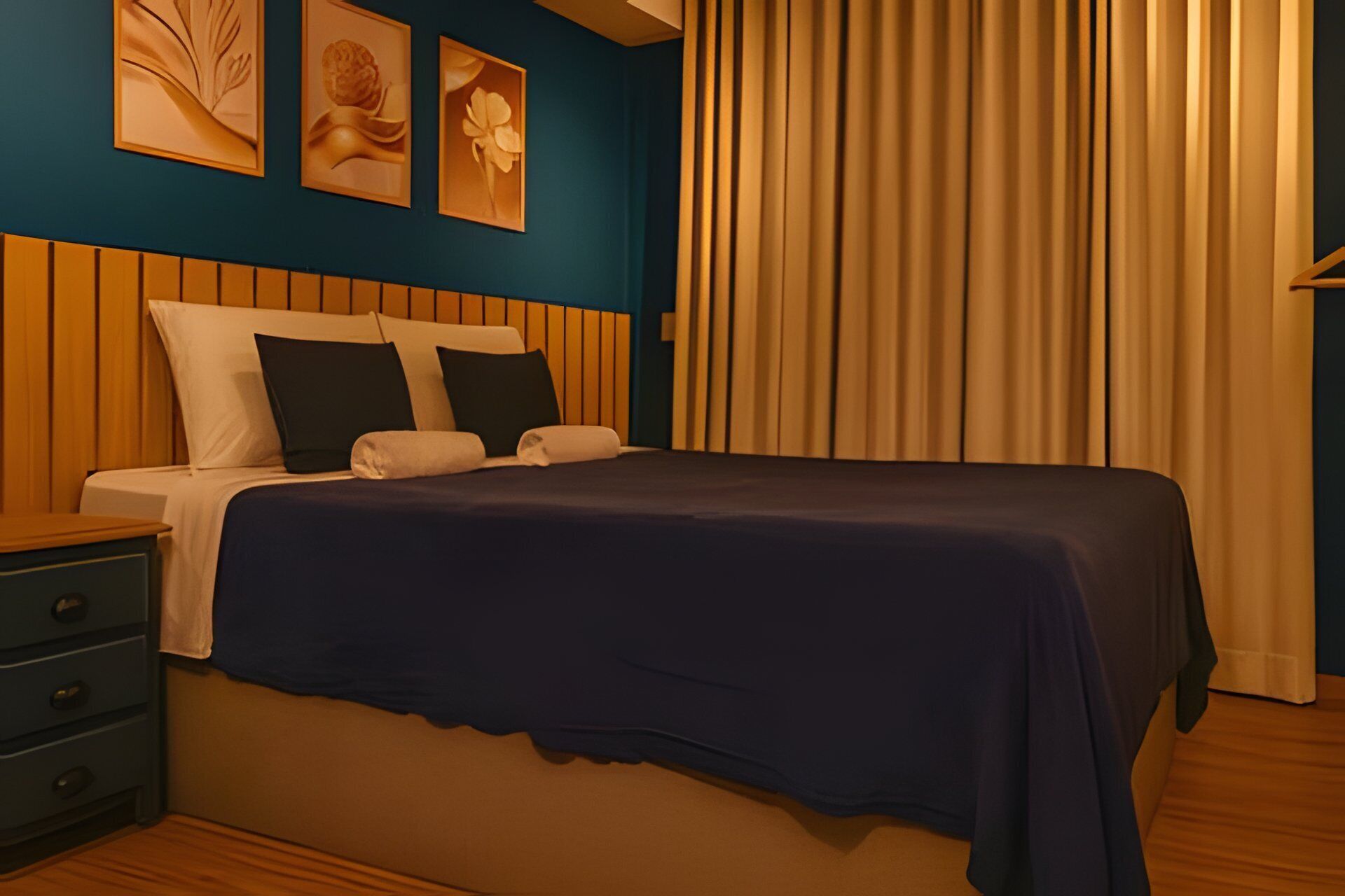 Una cama bien hecha con una colcha azul oscuro, un cabecero de madera y una mesita de noche con cajones.