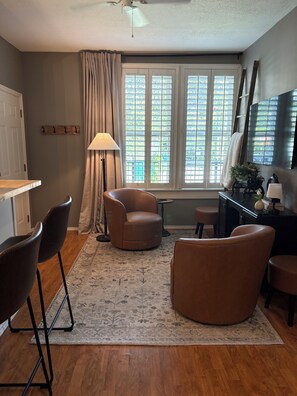 A modern living room with a sofa, chairs, a coffee table, a lamp, a TV, and a window with blinds.