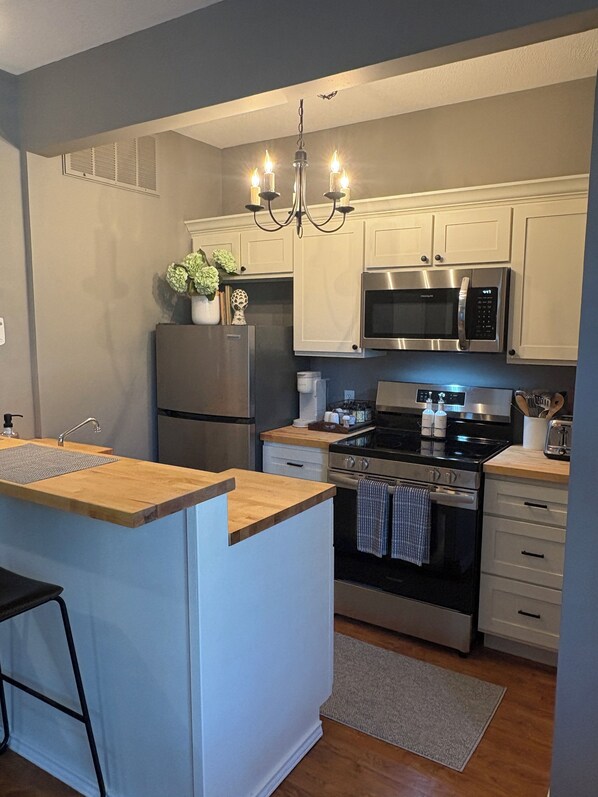 A modern kitchen with a central island, stainless steel appliances, and a chandelier.
