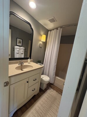 A bathroom with a sink, mirror, toilet, and shower curtain.
