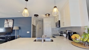 Et moderne køkken med en central ø, rustfrie hårde hvidevarer og hængende lamper.