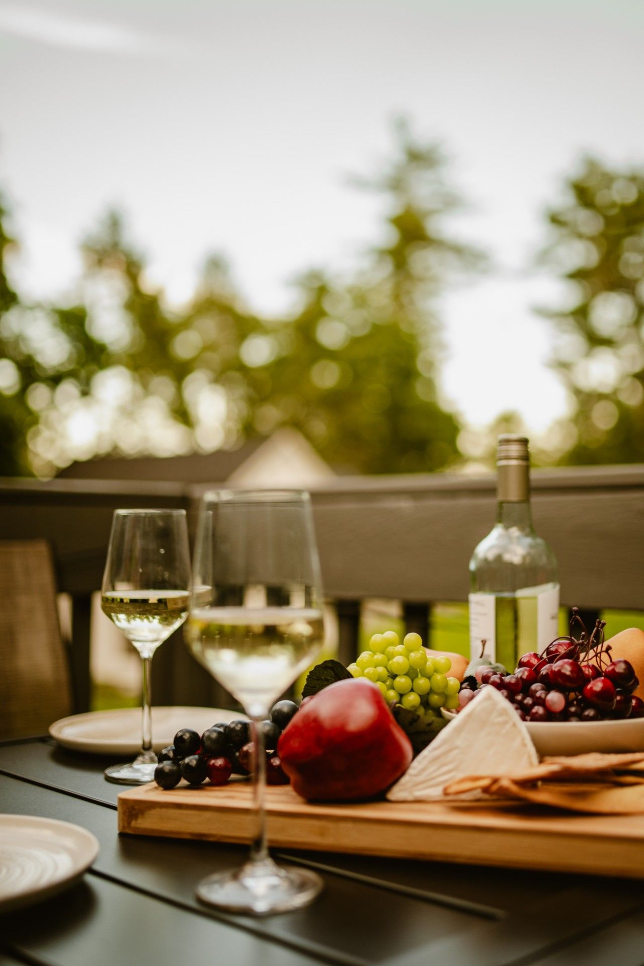 Une table avec une bouteille de vin blanc, deux verres et une variété de fruits et de fromages.