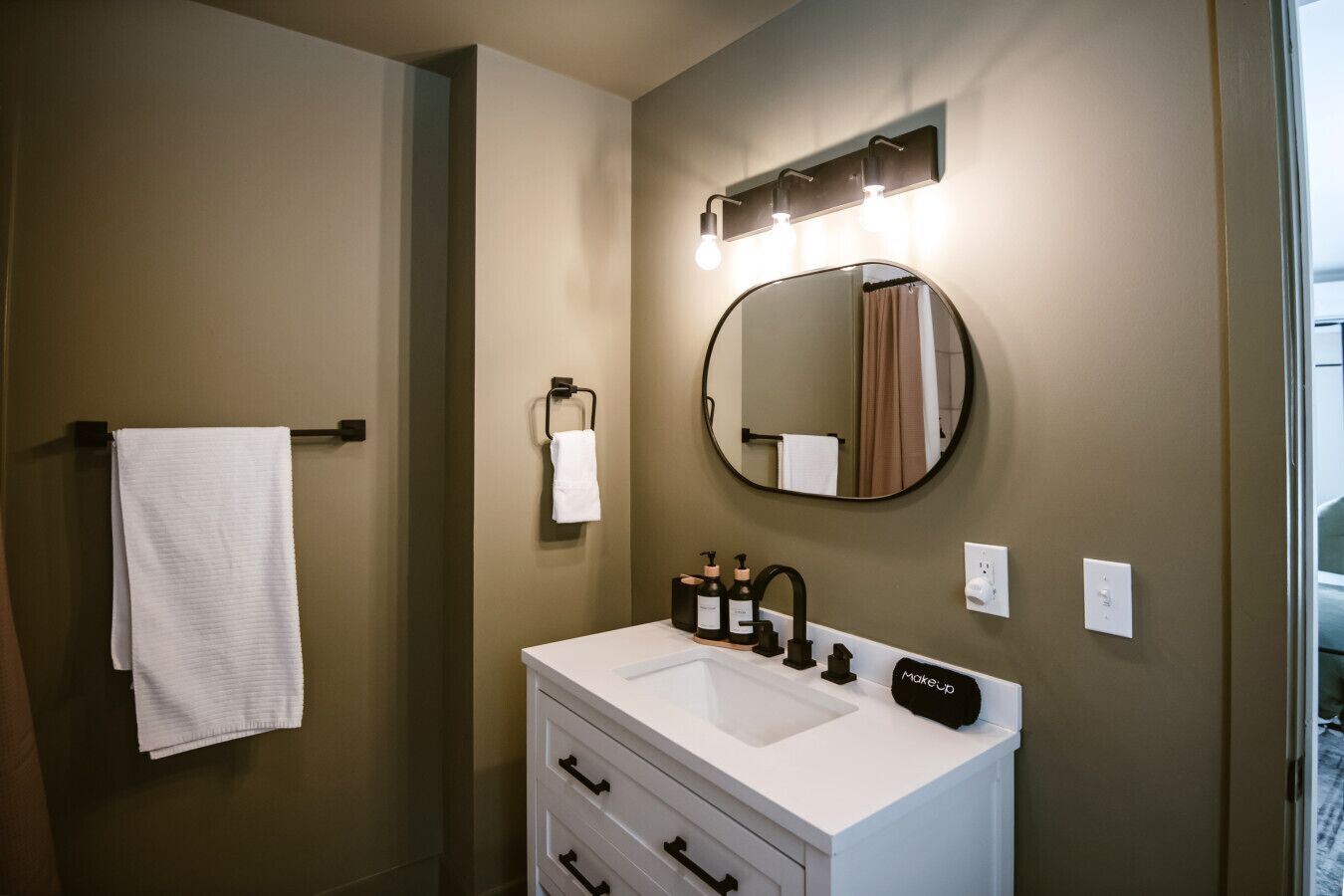 A bathroom with a white vanity, a round mirror, and a towel rack.