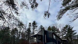 A two-story cabin with a balcony, surrounded by a forest and snow-covered ground. - Modern Cabin with Fire Pit | Big Bear Ski & Hiking (Eldred)