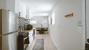 A modern kitchen with white cabinets, a stainless steel refrigerator, and a dining area with a table and chairs. - Modern Cabin with Fire Pit | Big Bear Ski & Hiking (Eldred)