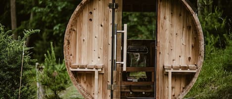 Una estructura de madera con forma de barril, con una puerta, un pequeño estante y una ventana.