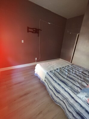 A bedroom with a bed, wooden flooring, a wall-mounted TV, and a power outlet.