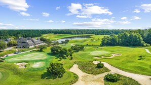 Un parcours de golf doté d’un club-house, d’un lac et entouré d’une forêt.