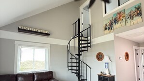 Ein Wohnzimmer mit einem braunen Ledersofa, einem gestreiften Teppich, einer schwarzen Wendeltreppe, einem Deckenventilator und einem Fenster mit Jalousien.