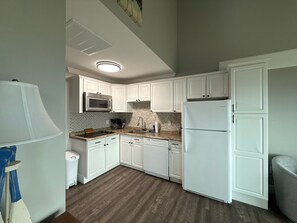 A kitchen with white cabinets, a microwave, a refrigerator, and a wooden floor. - Oceanfront 3-bedroom townhome with AC & outdoor shower in North Topsail Beach (North Topsail Beach)