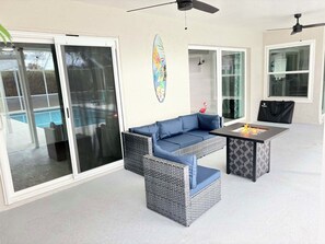 Un espace patio extérieur avec un canapé bleu, une table dotée d’un foyer et une planche de surf décorative accrochée au mur.