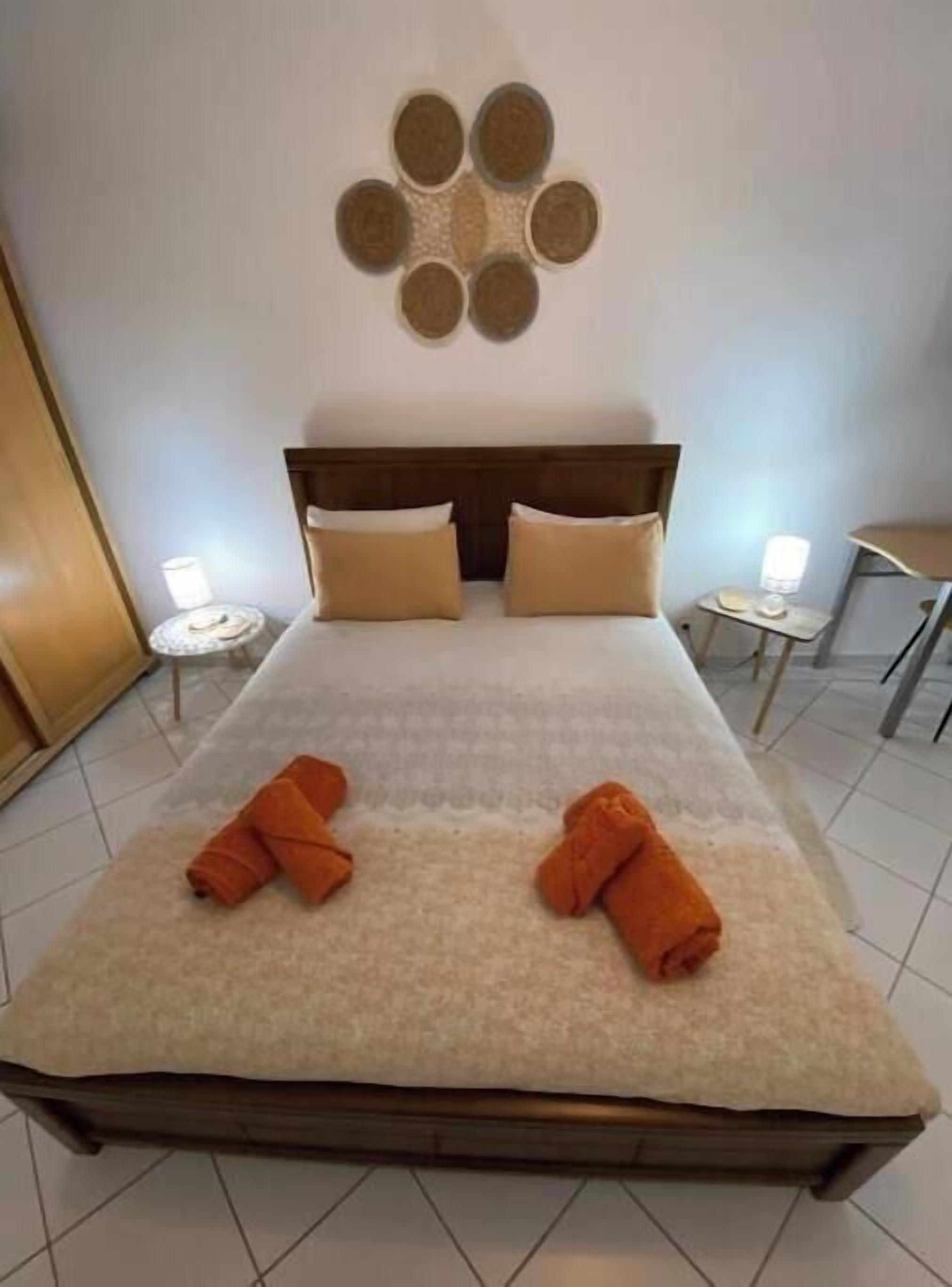 A hotel room with a bed, two pillows, a headboard, a wall decoration, and two folded towels on the bed.