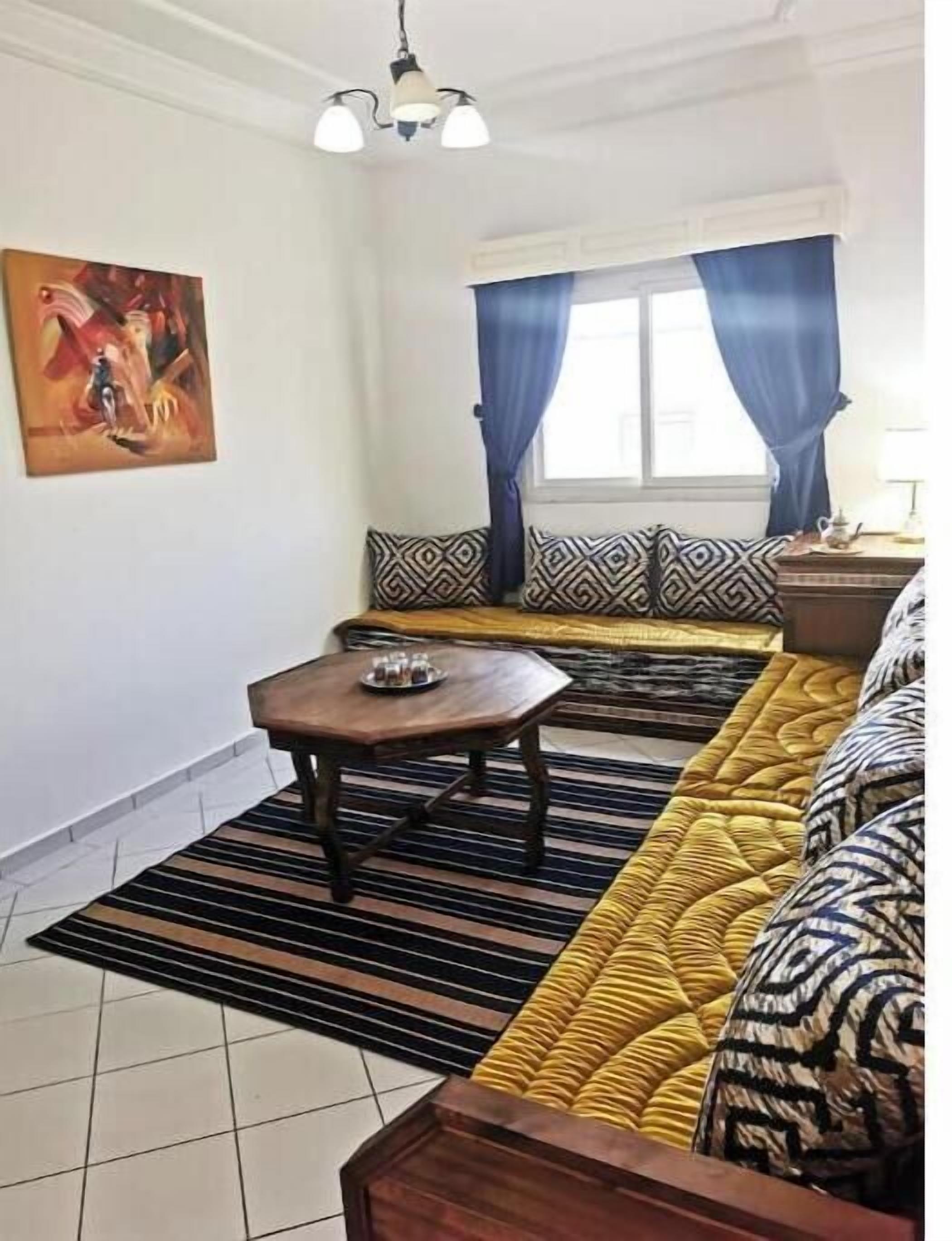 Een woonkamer met een bank, een salontafel, decoratieve kussens, een schilderij aan de muur, en een raam met gordijnen.