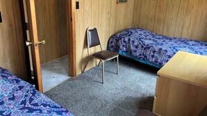 A room with two beds, a chair, a small table, and a wooden door.