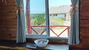 Ein Zimmer in einer Holzhütte mit Fenster, Vorhängen, die mit Schleifen gebunden sind, einer Meerfarn-Dekoration und einer Schale auf der Fensterbank.