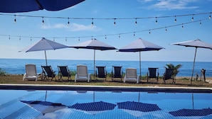 Ein Pool mit Liegestühlen und Sonnenschirmen, mit Blick auf ein Gewässer.