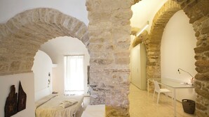 Una habitación con arcos de piedra, una cama, un escritorio y una silla.
