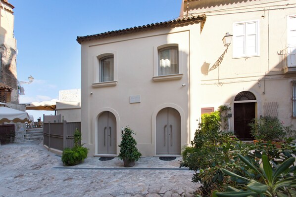 A building with a stone courtyard, arched doorways, and potted plants.