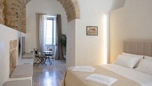 A hotel room with a stone archway, a bed with white linens, a small table with chairs, and a window with curtains. - TROPEA VETERA LuxuryHome-Casa Forno1638 (Tropea)