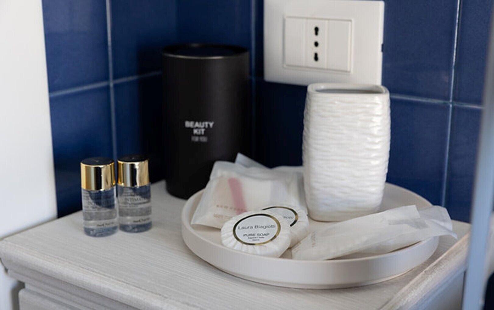 A bathroom vanity with a white tray holding a bar of soap, a bottle of lotion, and a black container labeled 'BEAUTY KIT.'