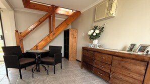Un coin repas avec un escalier en bois, une table à manger avec des chaises, un meuble avec des tiroirs et un sol carrelé.