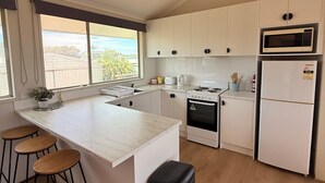 Une cuisine moderne avec des meubles blancs, un îlot central doté de tabourets, une cuisinière, un four à micro-ondes et un réfrigérateur.