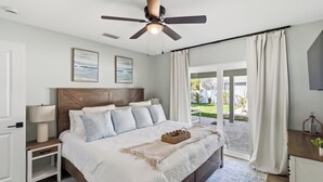 Une chambre à coucher comprenant un lit, des tables de chevet, un ventilateur de plafond, une fenêtre avec des rideaux et une vue sur l’extérieur.