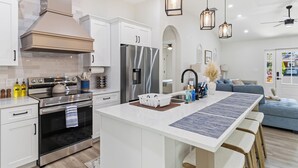 Une cuisine moderne dotée d’appareils électroménagers en acier inoxydable, d’un îlot central, de luminaires suspendus et offrant une vue sur l’espace de vie.