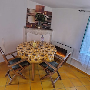 Ein runder Esstisch mit einer blumigen Tischdecke, Holzsesseln, einer Blumenvase und einem Kamin.
