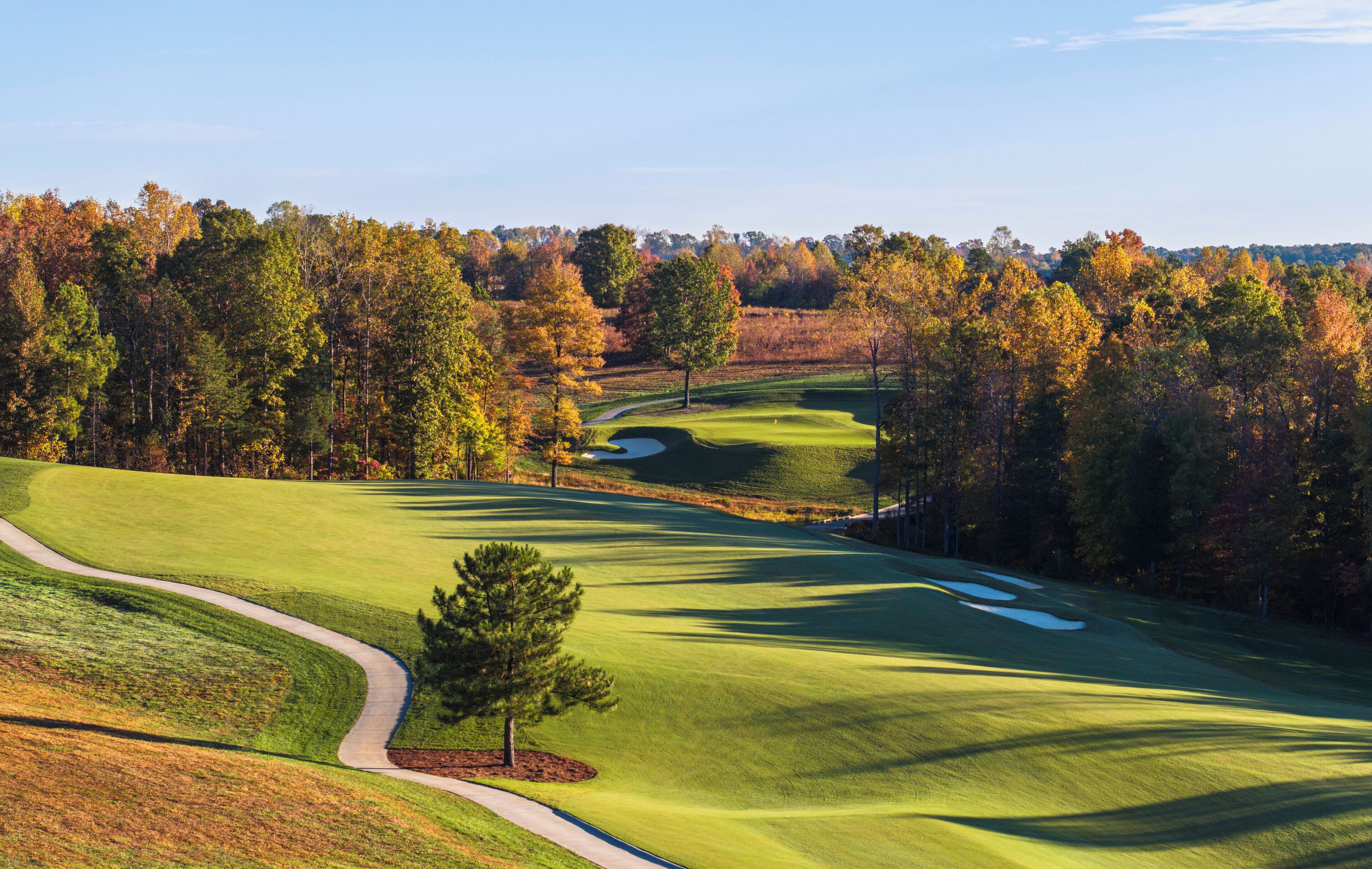 A golf course with a winding path, sand bunkers, and a variety of trees in autumn colors.