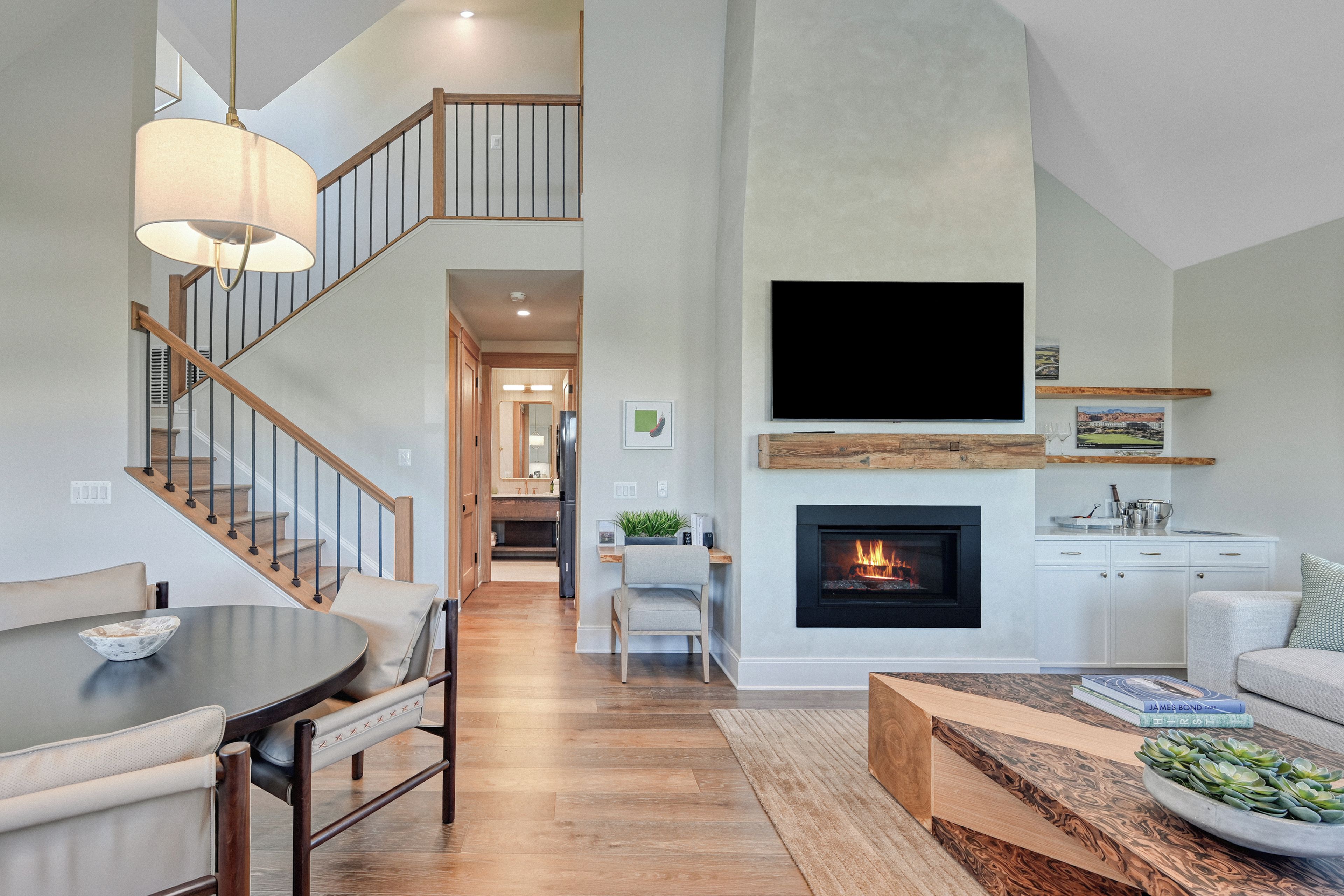 A spacious living area with a fireplace, a flat-screen TV, and a staircase leading to an upper level.