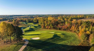A golf course with a winding path, sand bunkers, and a backdrop of autumn-colored trees.