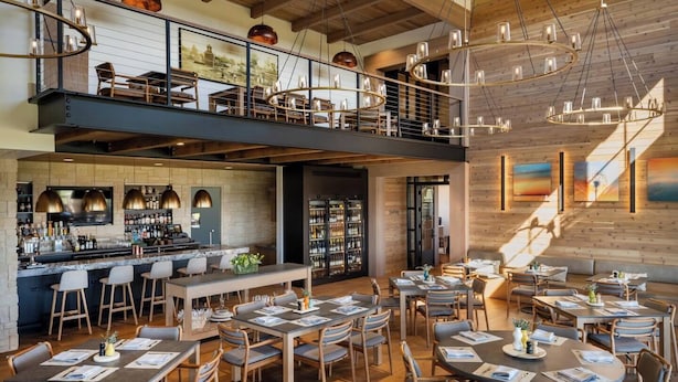 Un restaurant à plusieurs niveaux avec des poutres en bois apparentes, un bar et des tables dressées pour accueillir les clients.