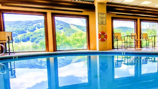 En swimmingpool med utsikt över ett skogbeklätt landskap genom stora fönster.