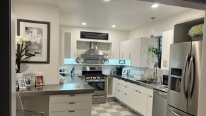 A modern kitchen with a central island, stainless steel appliances, and a checkered floor. - Eclectic Clarksville Austin Sauna Cold Plunge Fitness.  Walk to ACL is 1.4 miles (Austin)