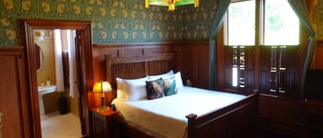 Ein Zimmer mit einem hölzernen Bett, einem Nachttisch mit Lampe, einem Spiegel und einem Fenster mit Vorhängen.