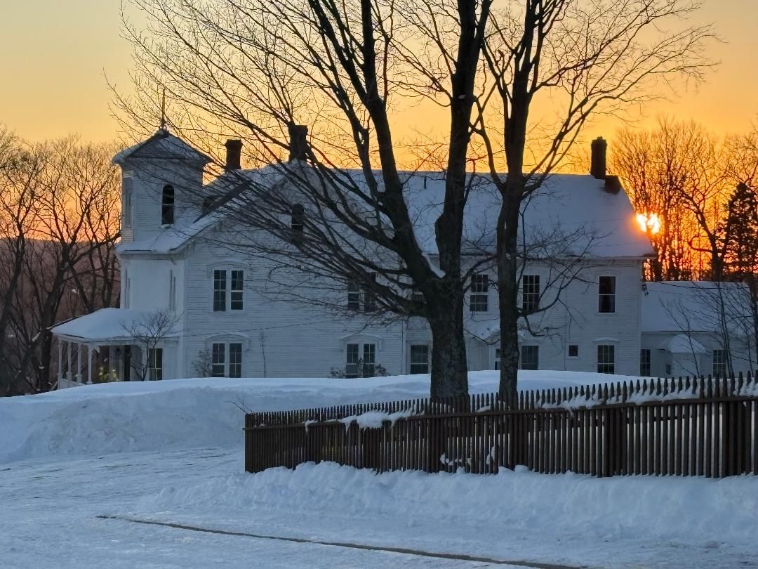 A large white house with a symmetrical facade, a central chimney, and a snow-covered yard.