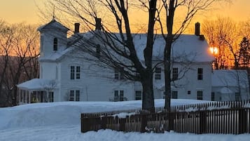 A large white house with a symmetrical facade, a central chimney, and a snow-covered yard.