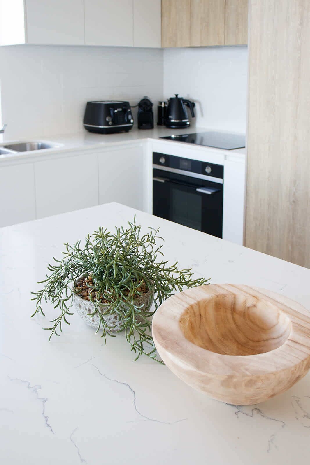 A kitchen with white cabinets, a black stove, and a countertop with a wooden bowl and a potted plant.
