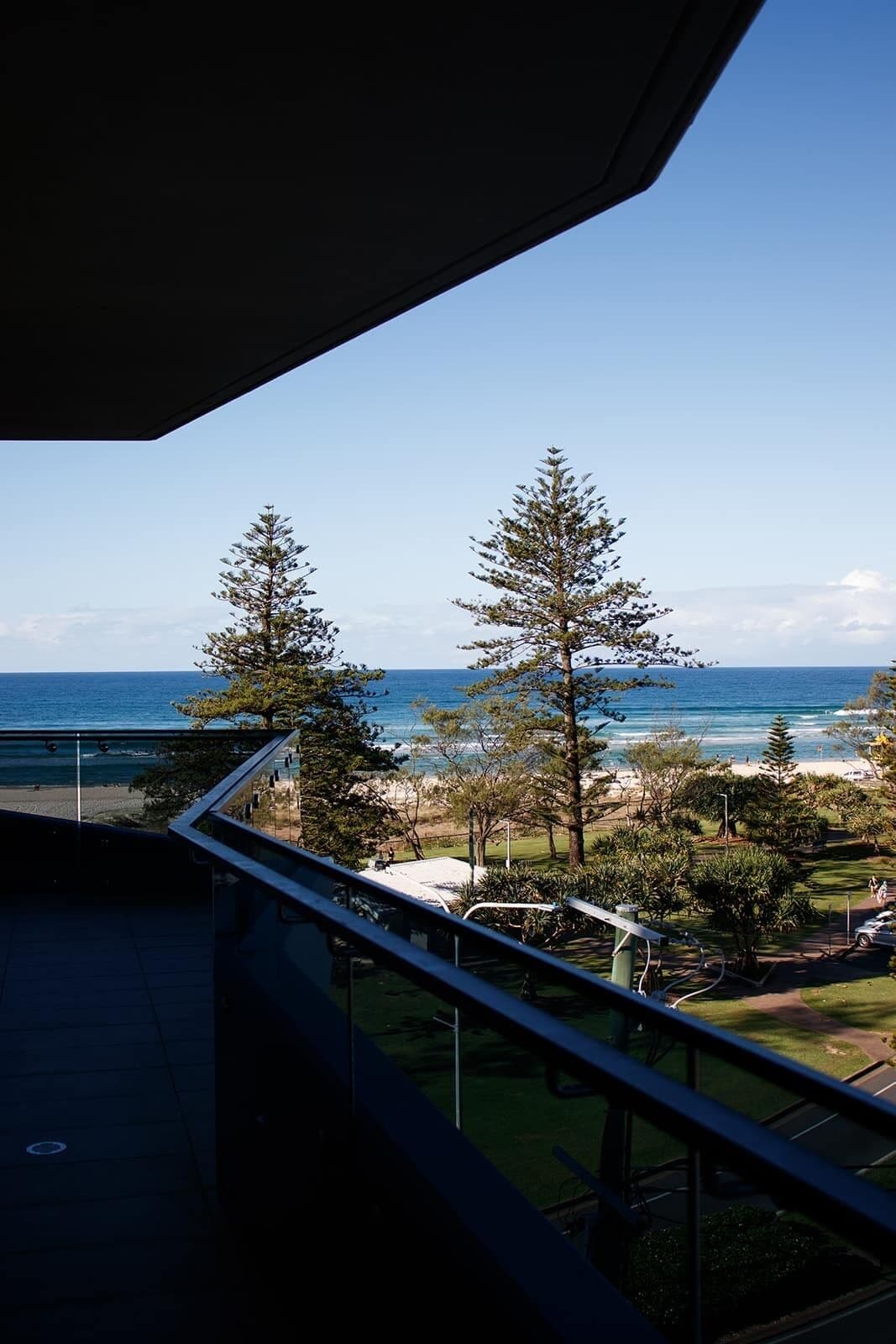 A balcony with a view of the ocean, trees, and a beach.