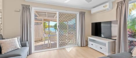 A living room with a ceiling fan, a flat-screen TV, and a sliding glass door leading to an outdoor area with a pool.