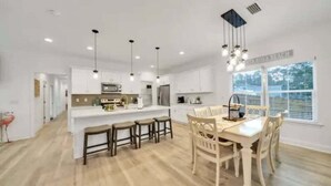 A modern kitchen with white cabinets, a central island, and pendant lighting. - Hot tub, The Tiki Hideaway, Close to Bay & Beach, Backyard Tiki Bar, Paddleboards (Santa Rosa Beach)