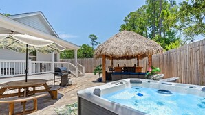 A backyard with a hot tub, a wooden deck, a barbecue grill, and a thatched-roof gazebo. - Hot tub, The Tiki Hideaway, Close to Bay & Beach, Backyard Tiki Bar, Paddleboards (Santa Rosa Beach)