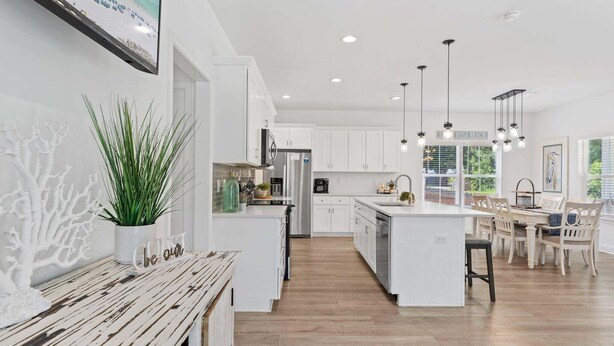 A spacious kitchen with white cabinetry, a central island, pendant lighting, and a dining area with a table and chairs. - Hot tub, The Tiki Hideaway, Close to Bay & Beach, Backyard Tiki Bar, Paddleboards (Santa Rosa Beach)