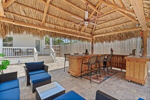 Eine Terrasse im Freien mit einer Holztresore, Korbmöbeln und einem Reetdach.