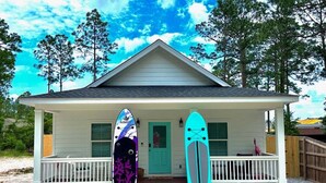 A house with a porch, two surfboards, and a door. - Hot tub, The Tiki Hideaway, Close to Bay & Beach, Backyard Tiki Bar, Paddleboards (Santa Rosa Beach)